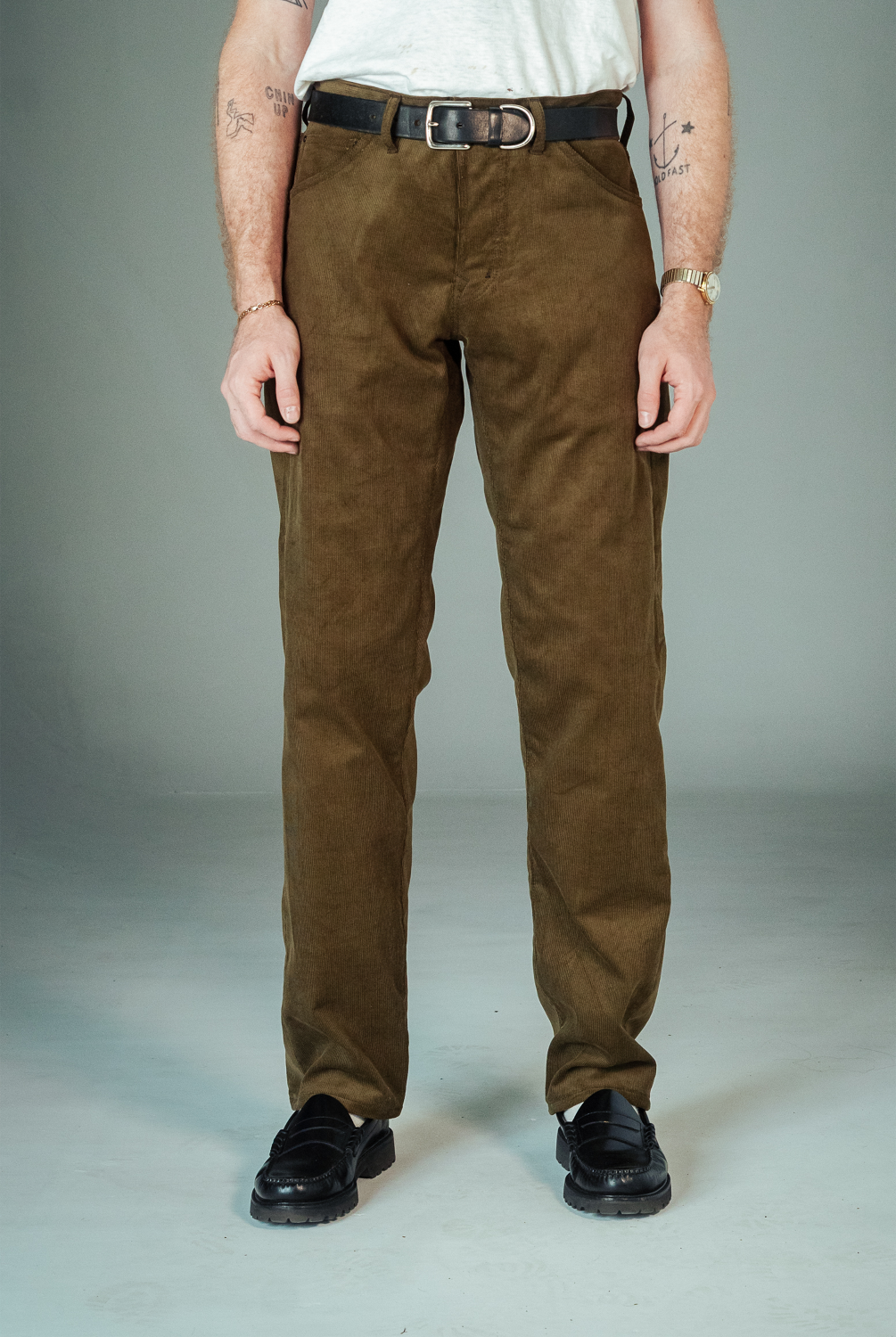 Person wearing brown pants and black shoes on a plain background