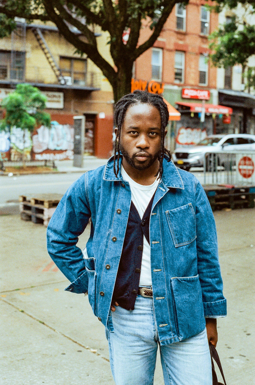 Man wearing a denim jacket and light blue jeans standing on a city street.
