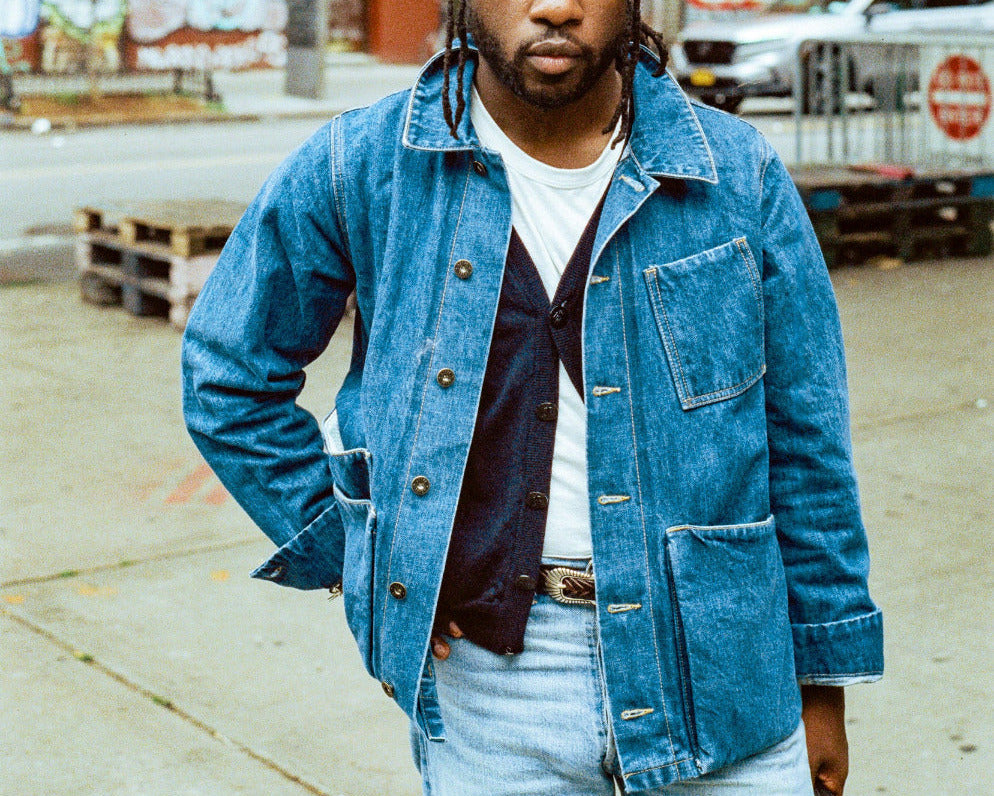Man wearing a denim jacket and light blue jeans standing on a city street.