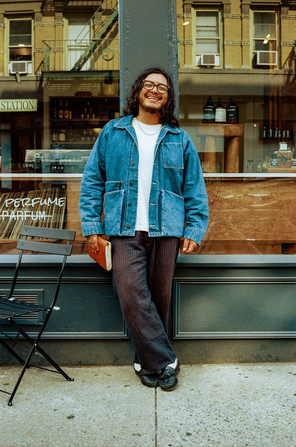 Man wearing a denim jacket standing on a sidewalk in an urban setting