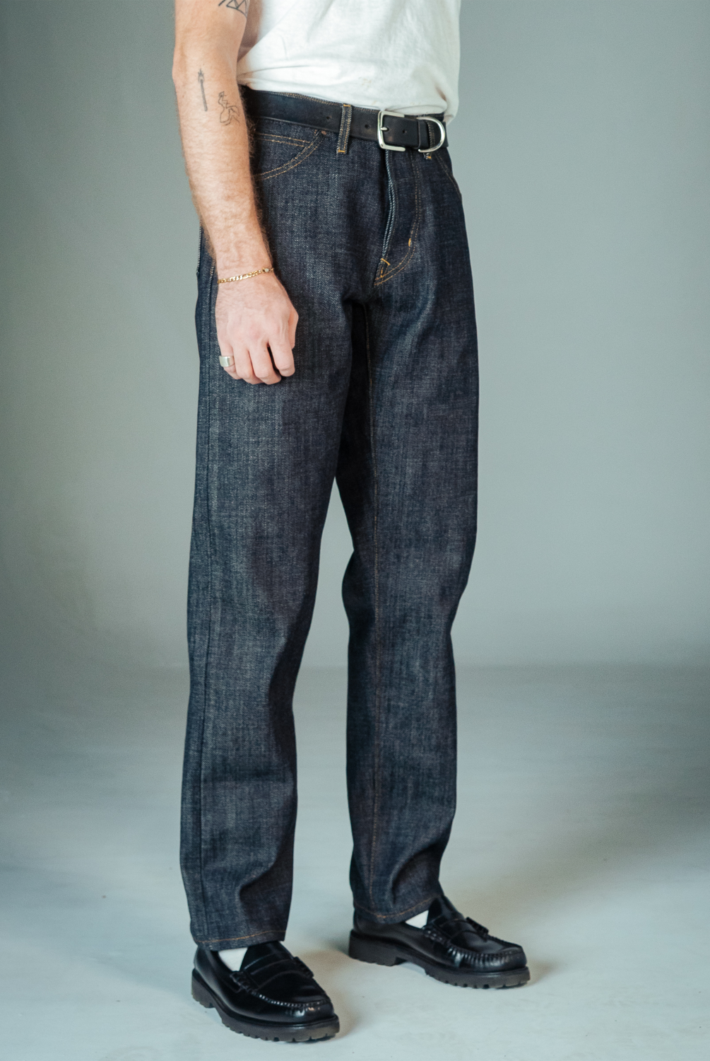 Person wearing dark blue jeans and black shoes on a plain background