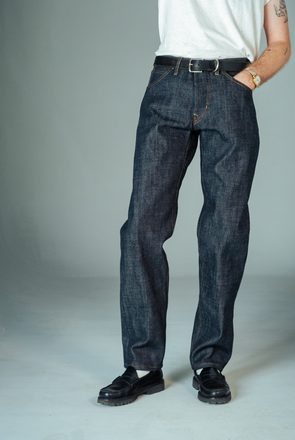 Person wearing dark blue jeans and black shoes on a plain background