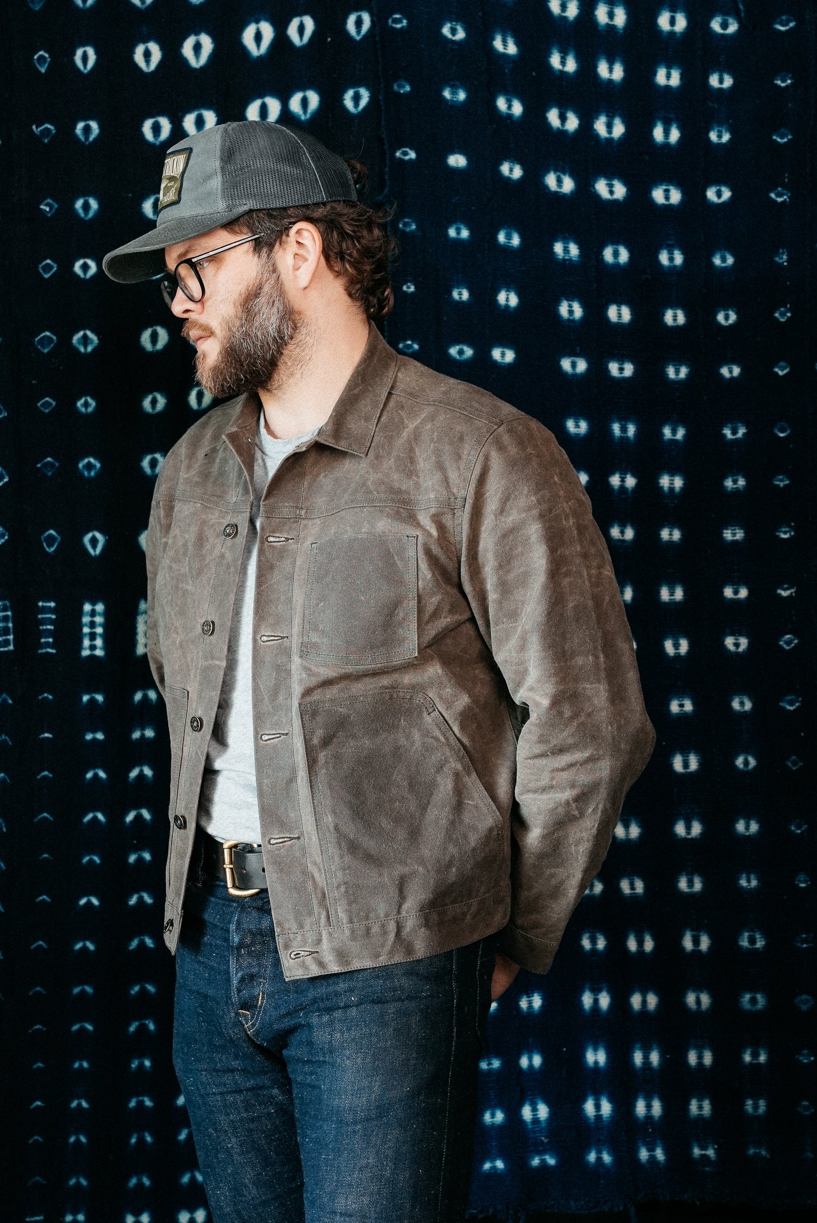 A person wearing a dark oak waxed canvas jacket with a crew neck and button-up front, paired with a white shirt and blue jeans.