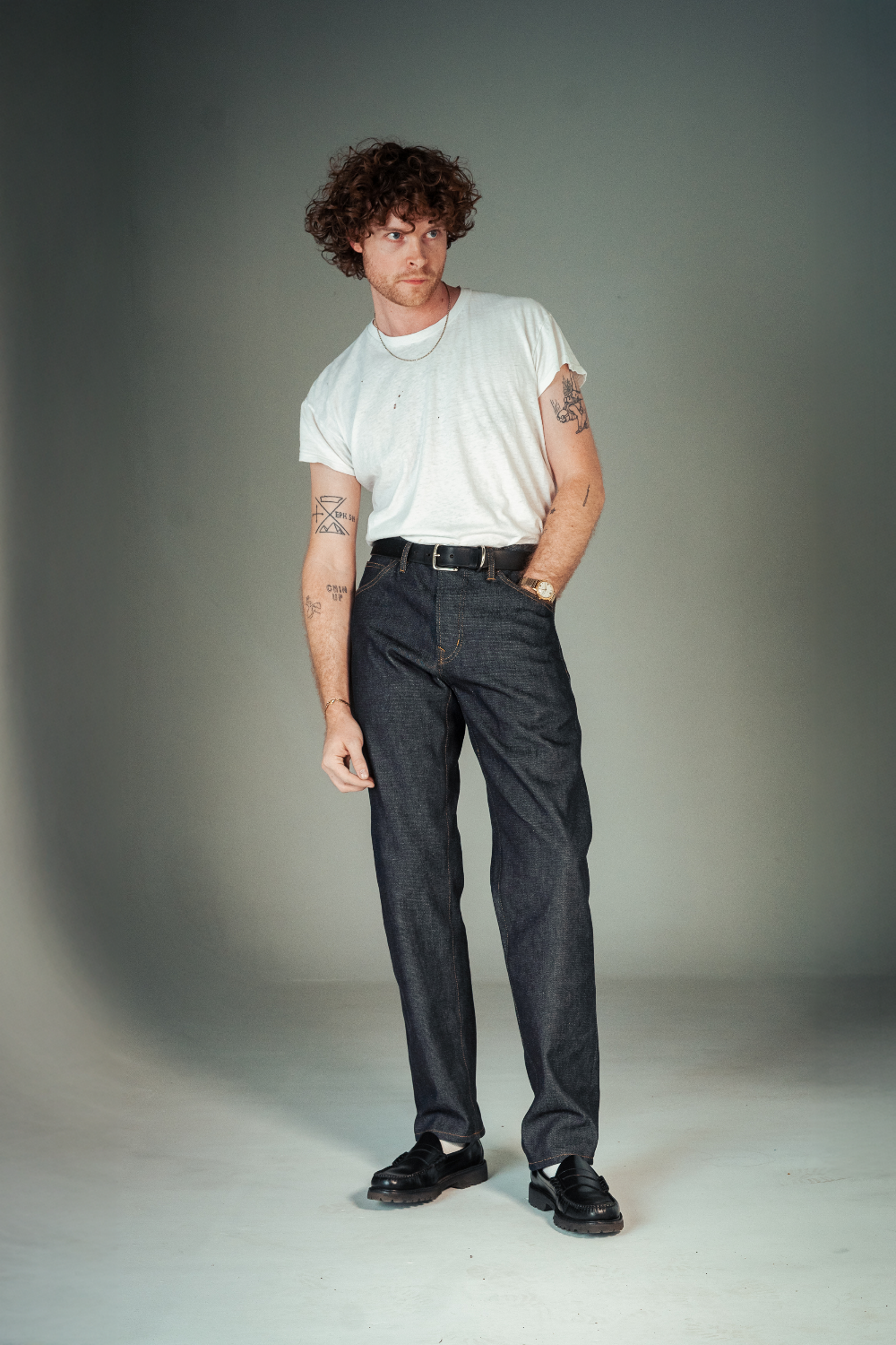 Man wearing a white t-shirt and dark jeans standing against a plain background