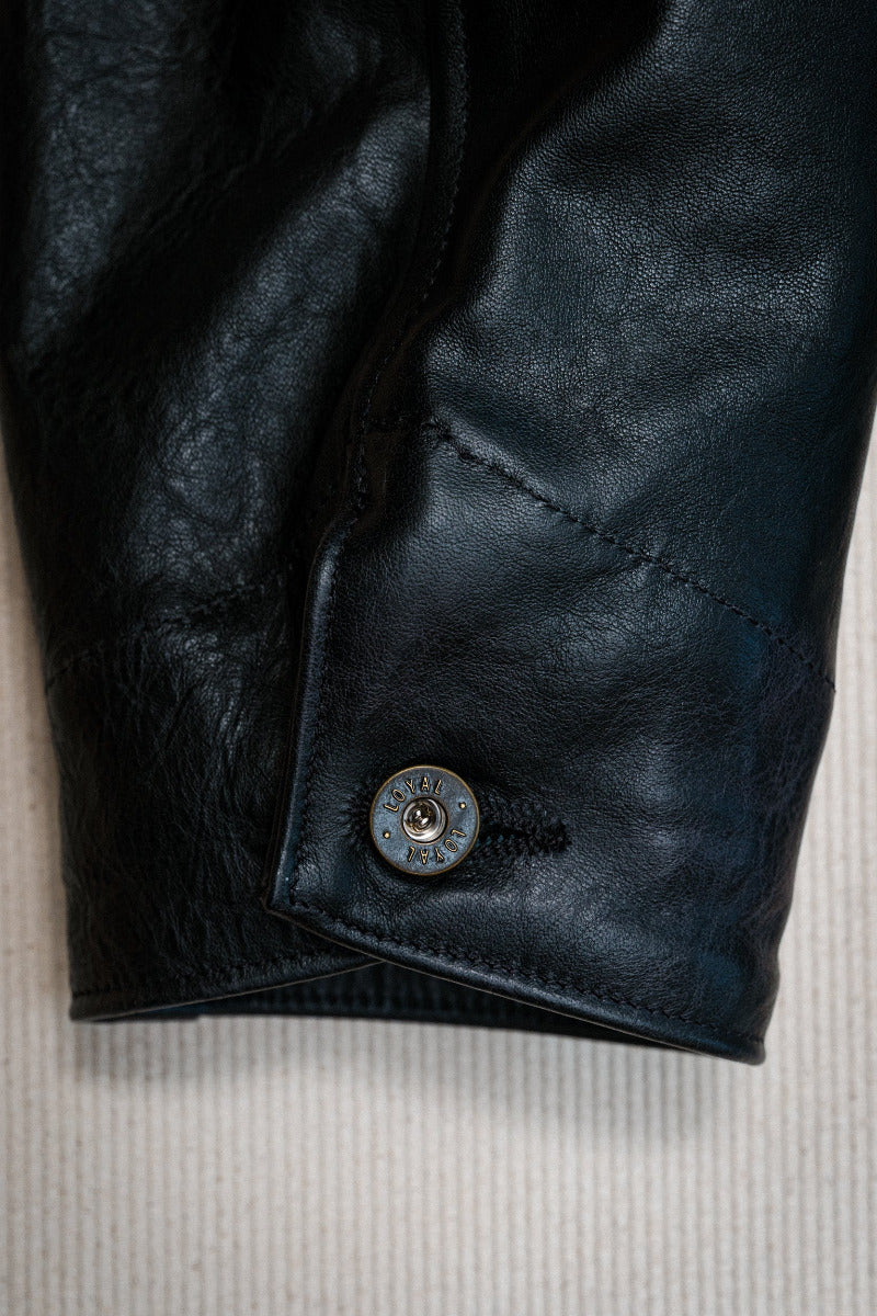 Close-up of a black leather jacket with a button on a textured beige background