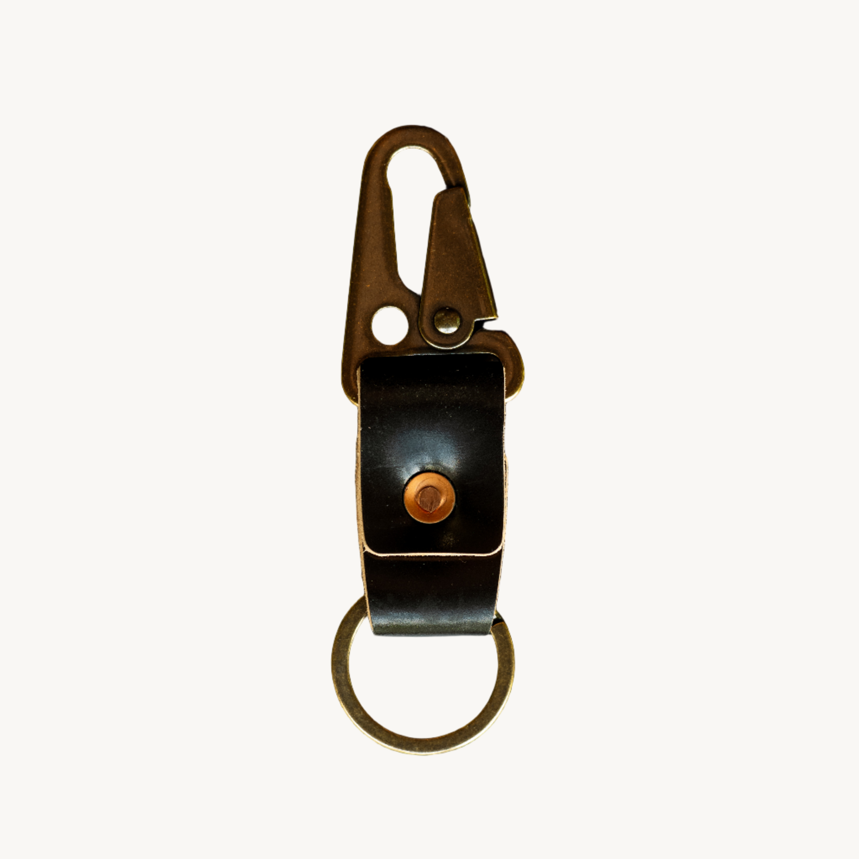 A black leather key clip with brass hardware, including a keyring and a lever clip, displayed against a dark textured background.