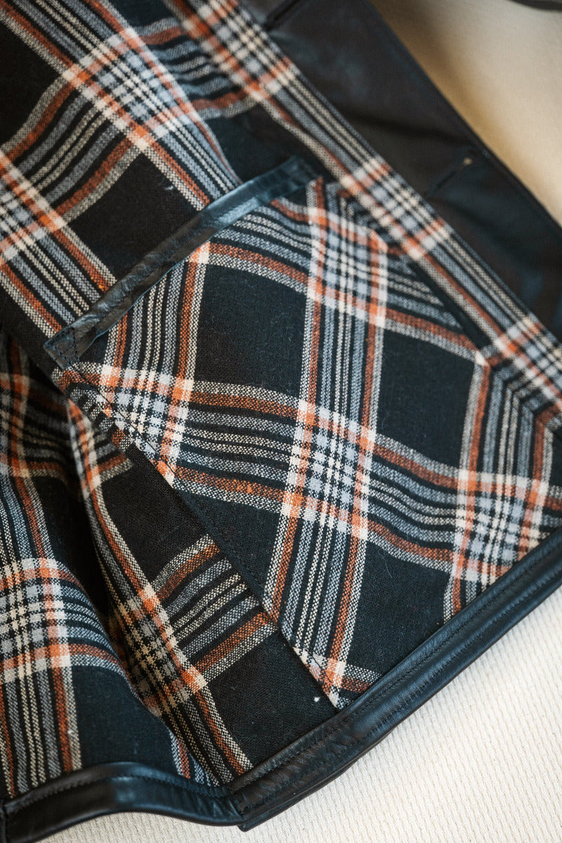 Plaid fabric with black, white, and orange pattern on a plain background